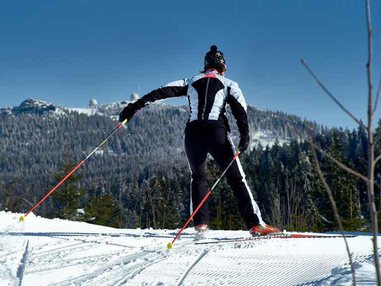 Ein Langläufer fährt durch die verschneite Landschaft mit Blick auf den Großen Arber im Bayerischen Wald.